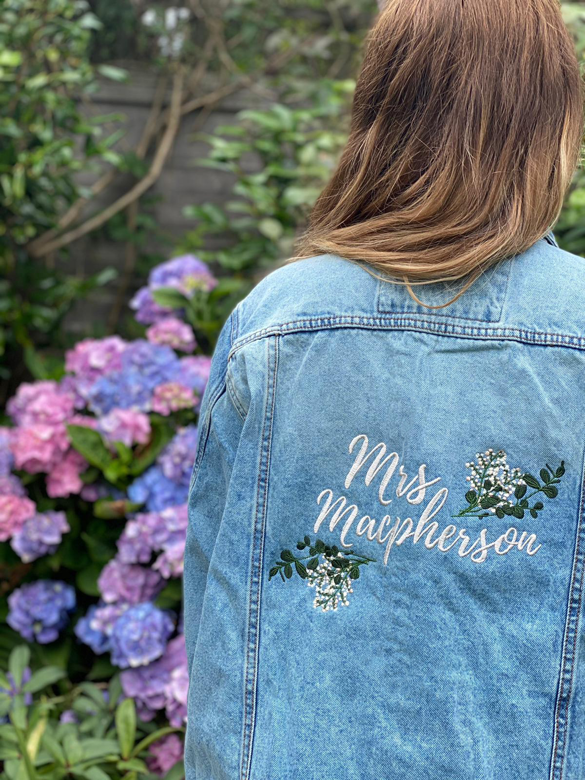 Personalised embroidered denim jacket with 'Mrs Macpherson' and floral design, garden background