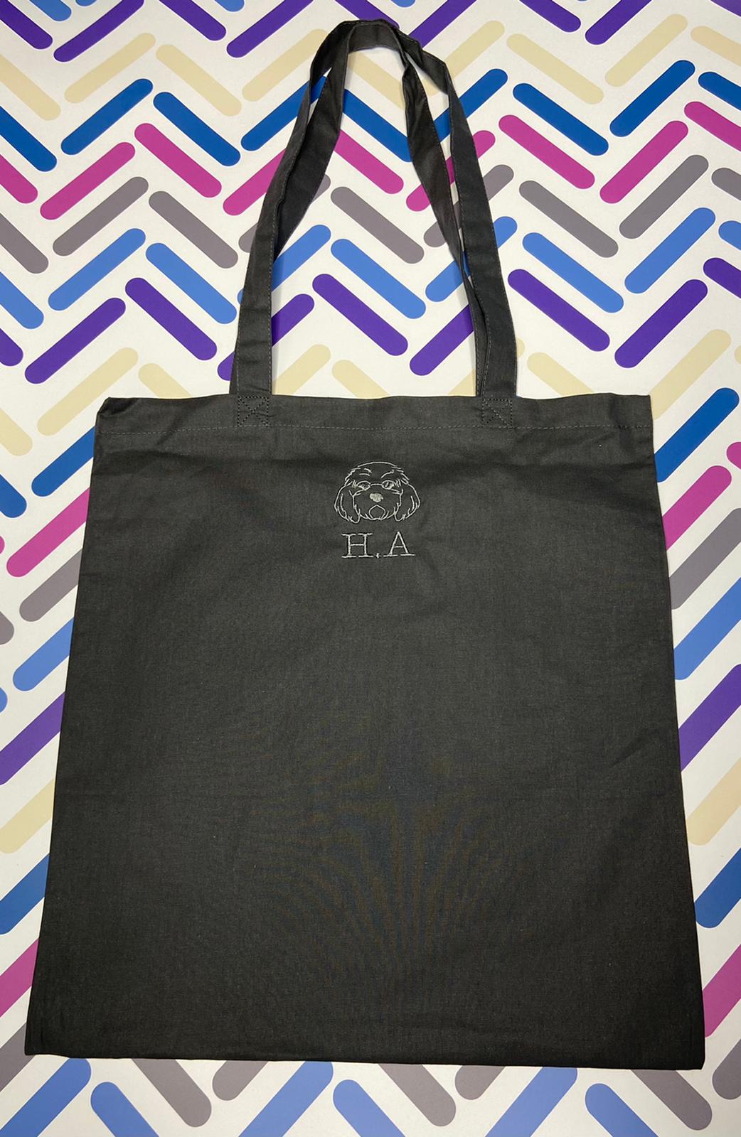 Personalised black tote bag with embroidered dog face and initials, on colorful background
