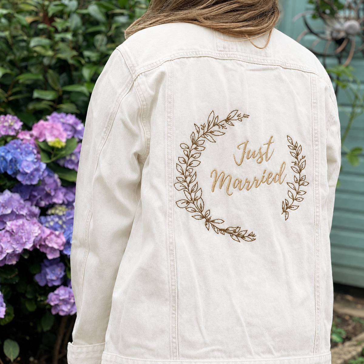 Model wearing white personalised Just Married embroidered bridal denim jacket in a garden